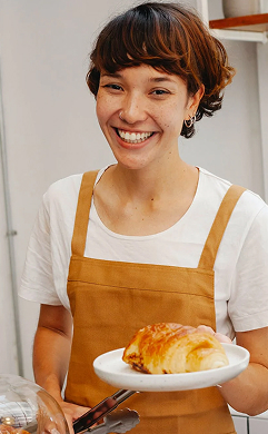 Шеф-кухар Настя із усмішкою тримає тарілку з круасаном 